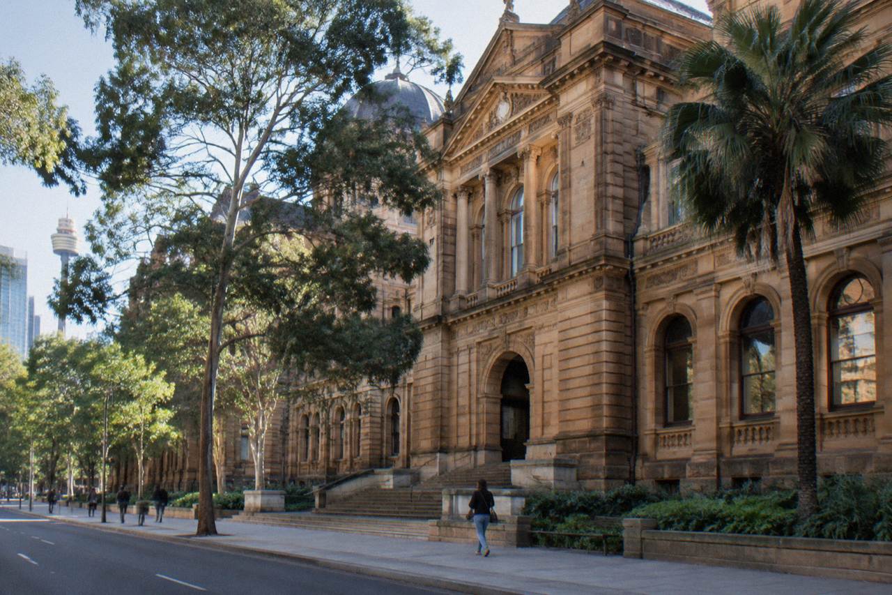 The colonnaded sandstone facade of the Art Gallery of NSW seen from Art Gallery Road, with visitors walking up the entrance steps.